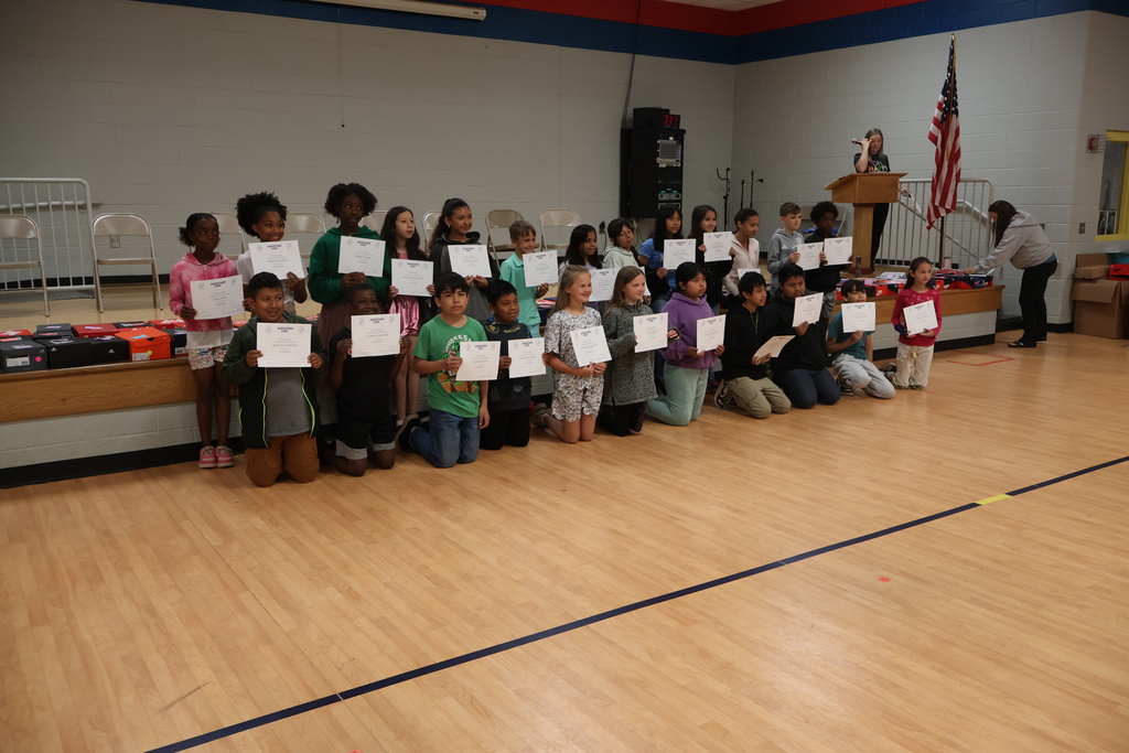 Students pose for a group picture in the gym with the certificates that they earned for the miles they ran. 