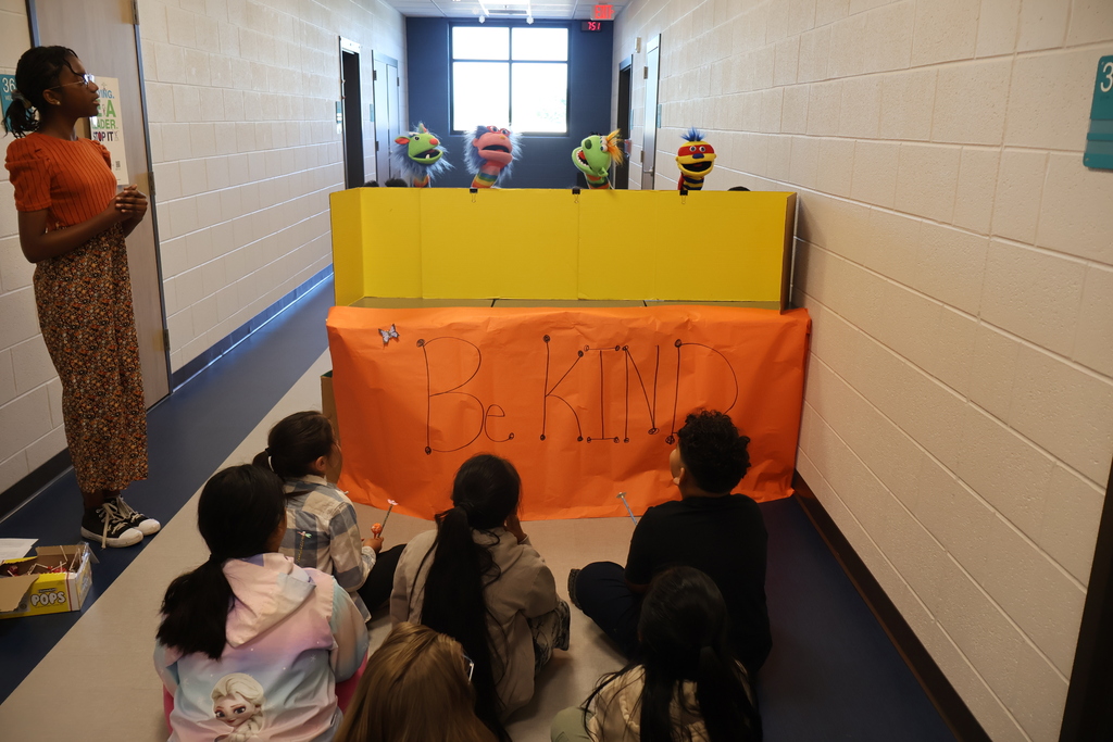 Students are sitting on the floor watching a puppet show.