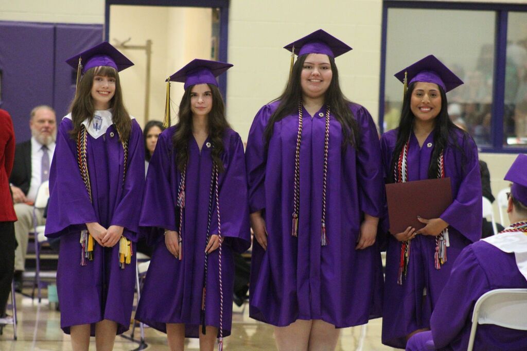 Four students are posed for a picture during honor's day wearing their caps and gowns. 