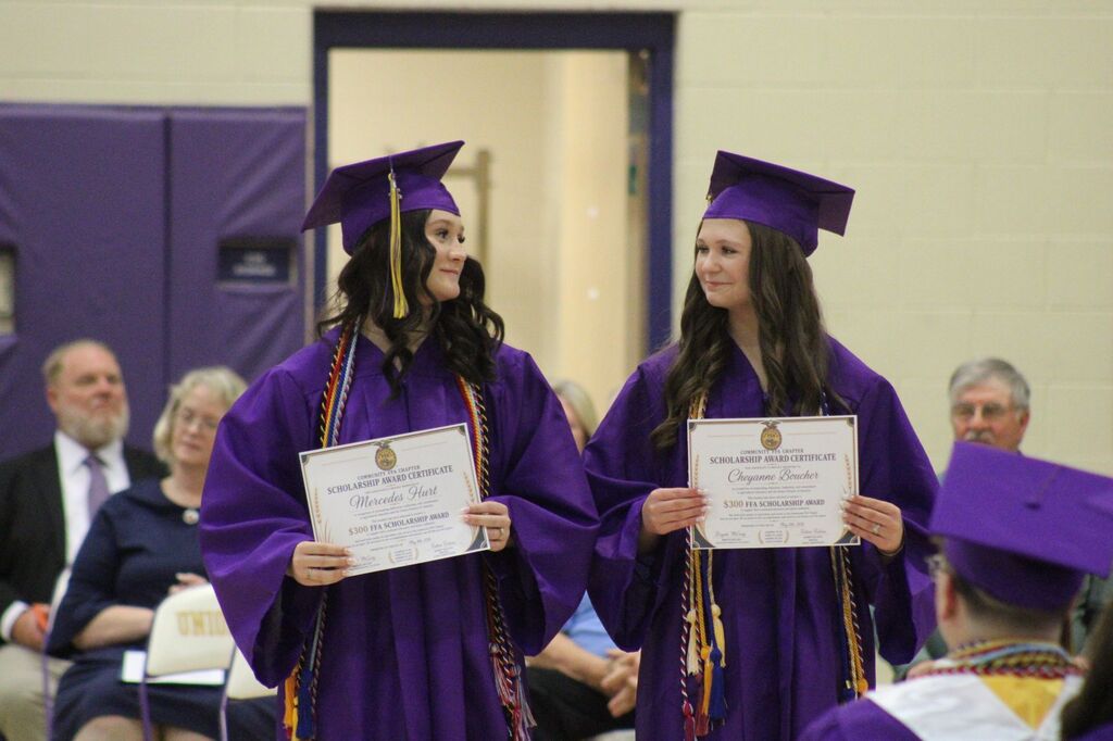 Two students are holding a scholarship certificate during honor's day wearing their caps and gowns. 