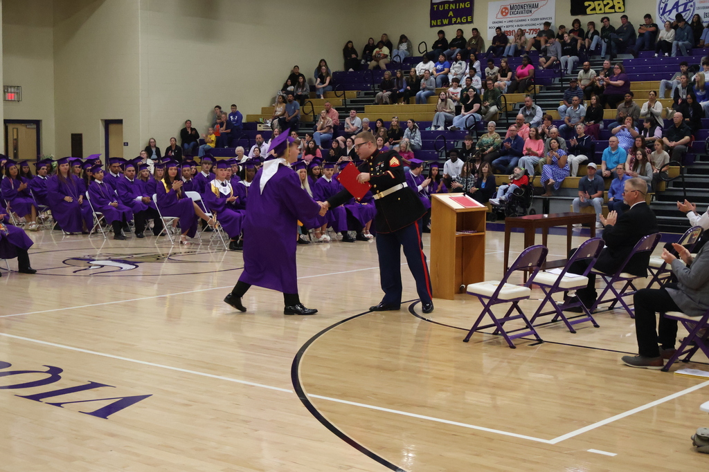 A student is shaking hands with a member of the military while be recognized for an award. 