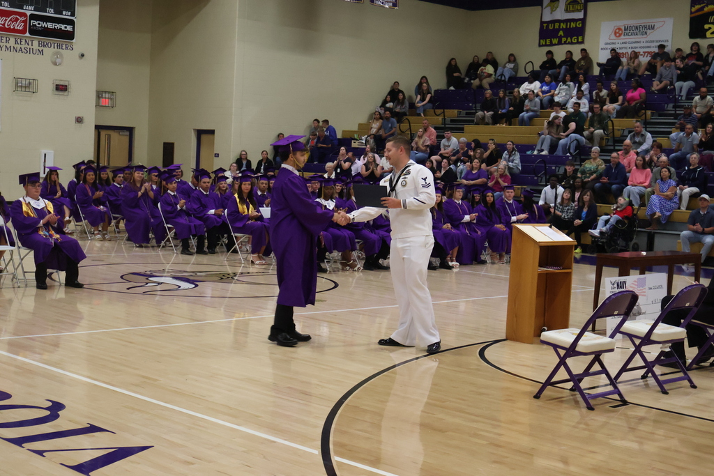 A student is shaking hands with a member of the military while be recognized for an award. 