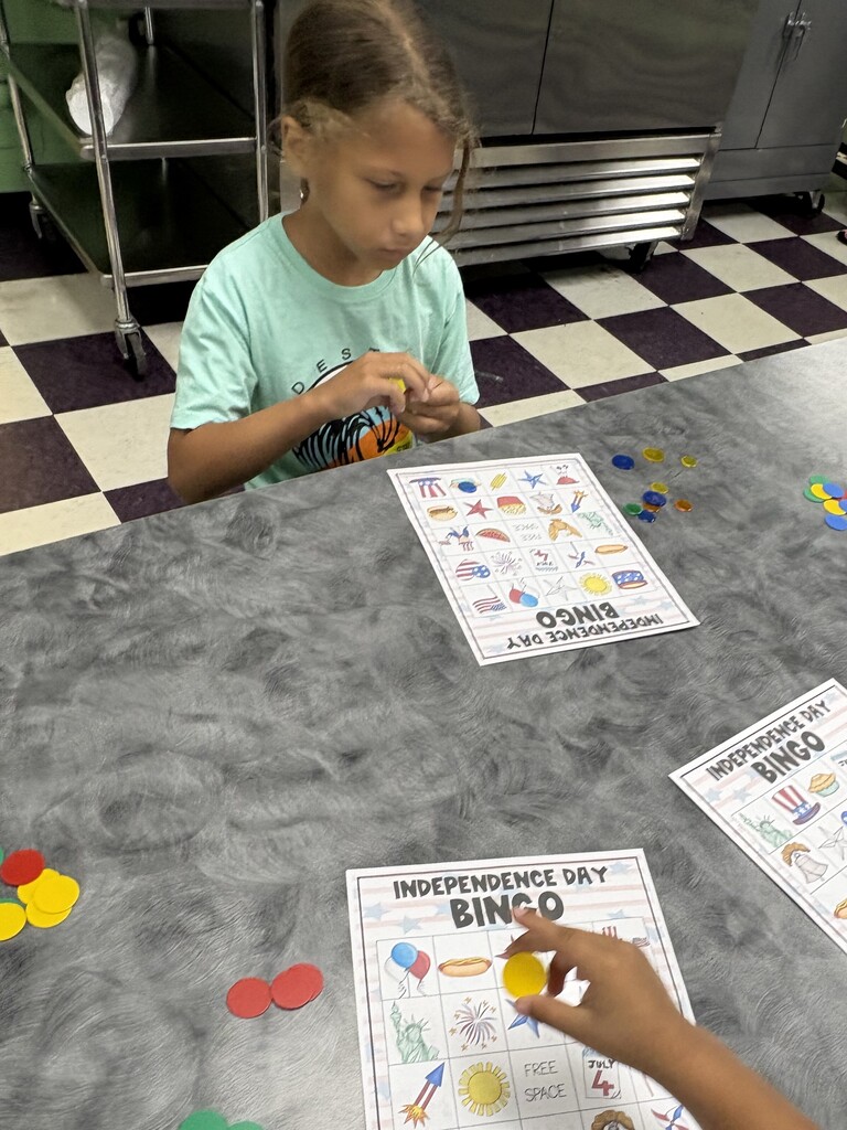 A student is sitting down at a table with their bingo sheet and the pieces that they will use to mark their sheets.