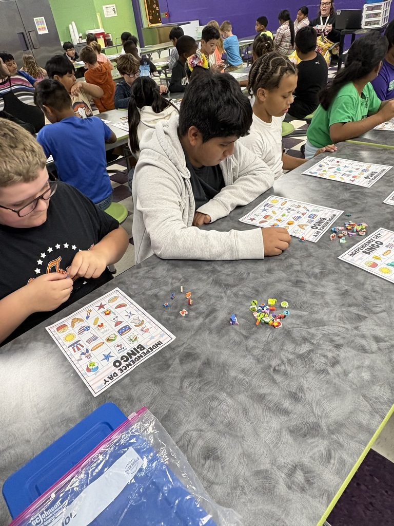 There are several students sitting down at a table with their bingo sheets and the pieces that they will use to mark their sheets while playing bingo.
