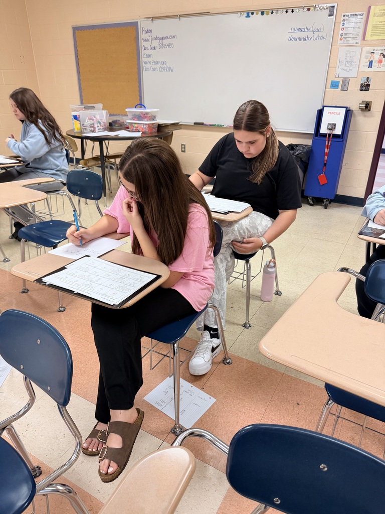 There are several students seated at their desks while doing work on a paper.