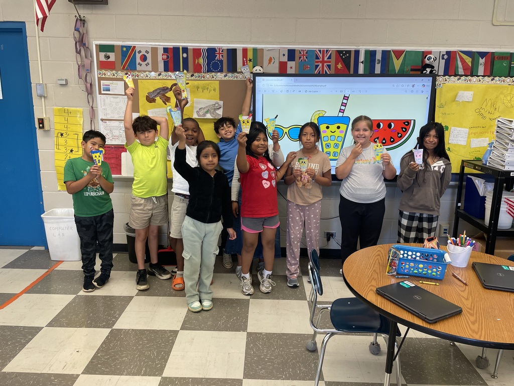 There is a group of students posing for a picture while holding paper lemonade cups that they colored and cut out.
