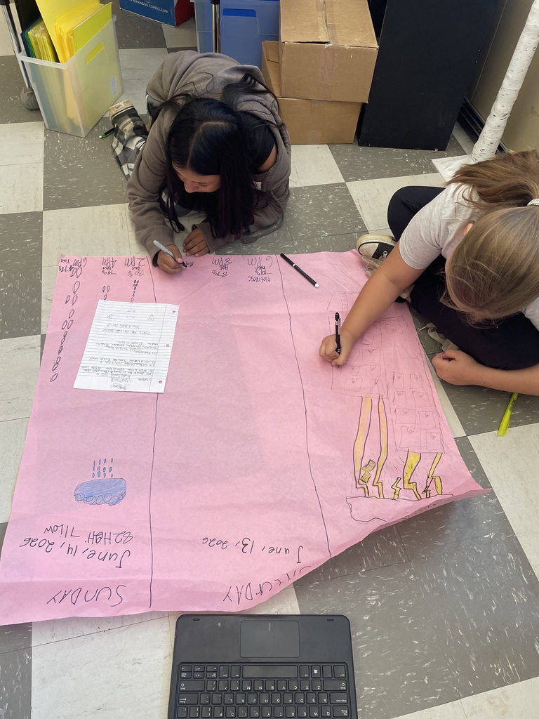 Students are on the floor coloring on a large piece of pink paper their predictions for this weekend's weather forecast.