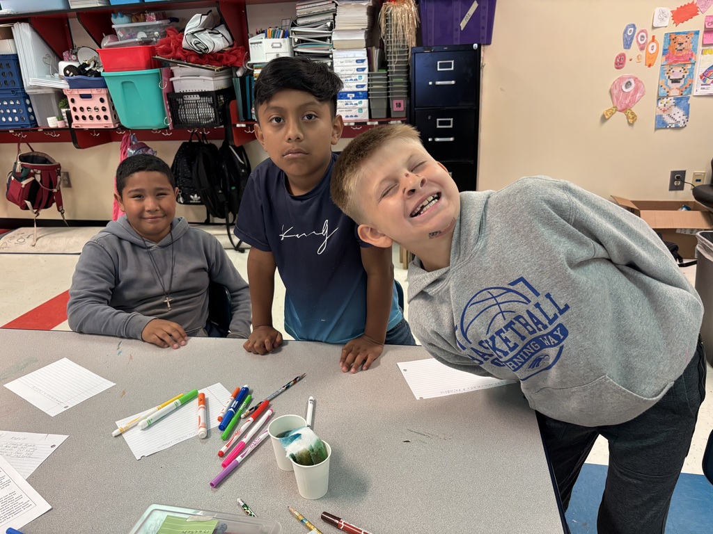 Three students are sitting down at a table with two cups of colored water as they participate in the walking water experiment. 