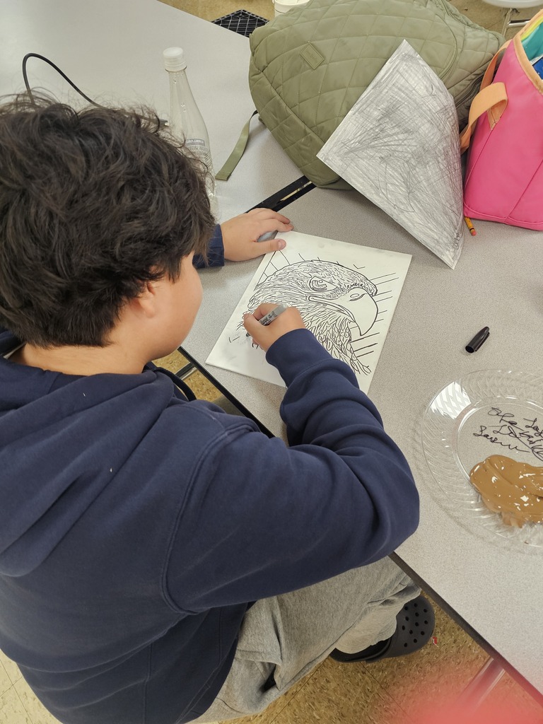 A student is sitting at a table painting his drawing that he made to celebrate America's 250th anniversary. 