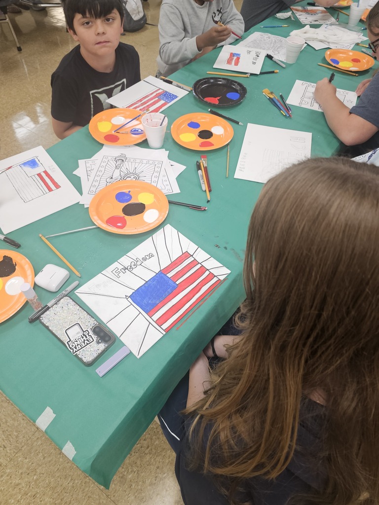 Several students are sitting at a table painting their drawings that they made to celebrate America's 250th anniversary. 