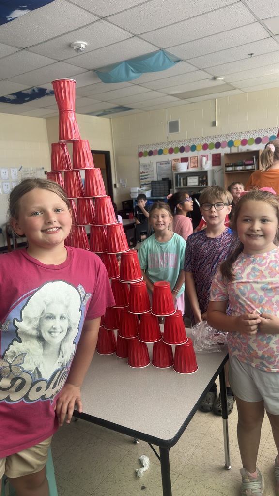 Several students are standing in front of a table where they stacked cups into a pyramid. 