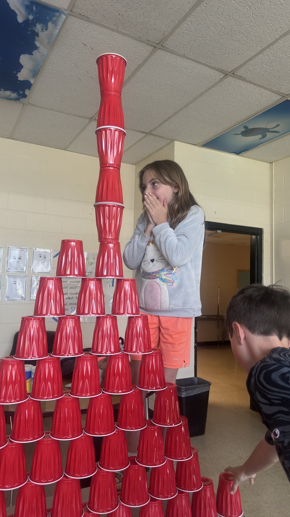 Several students are standing in front of a table where they stacked cups into a pyramid. 