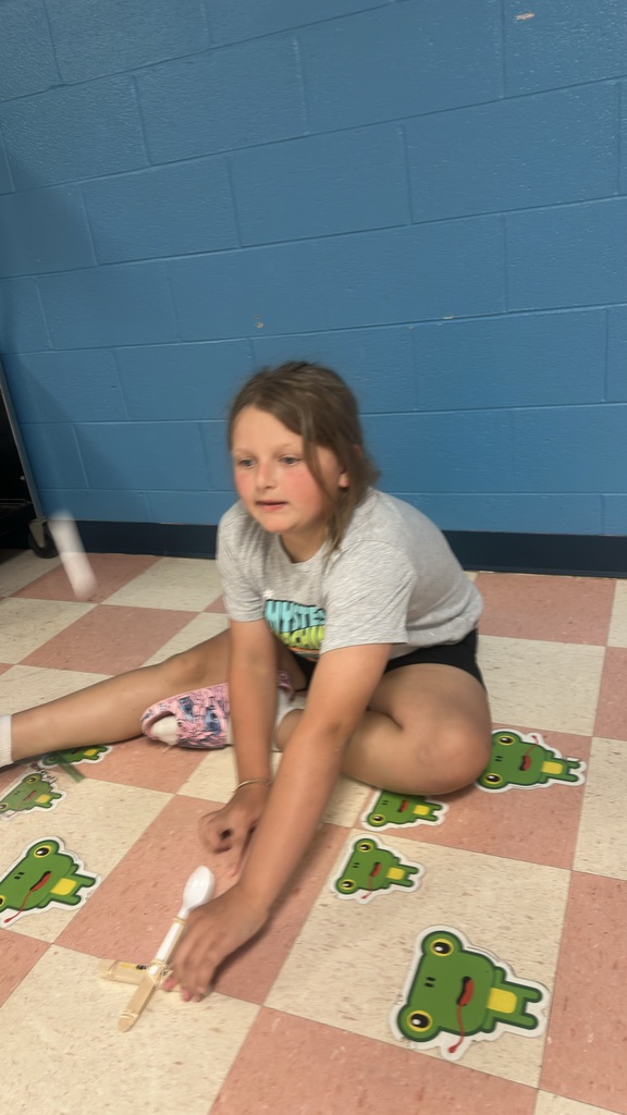 A student is sitting on the floor trying out the catapult she made. 