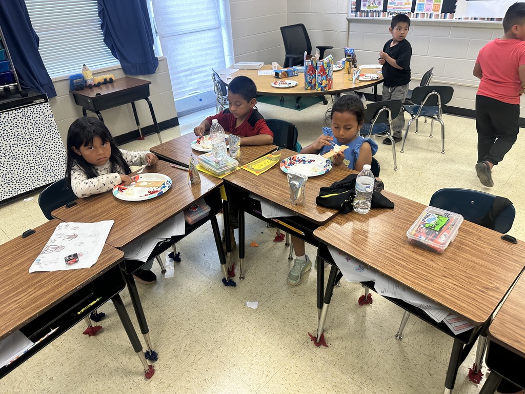 Three students are sitting at their desks decorating graham crackers to look like the American flag.