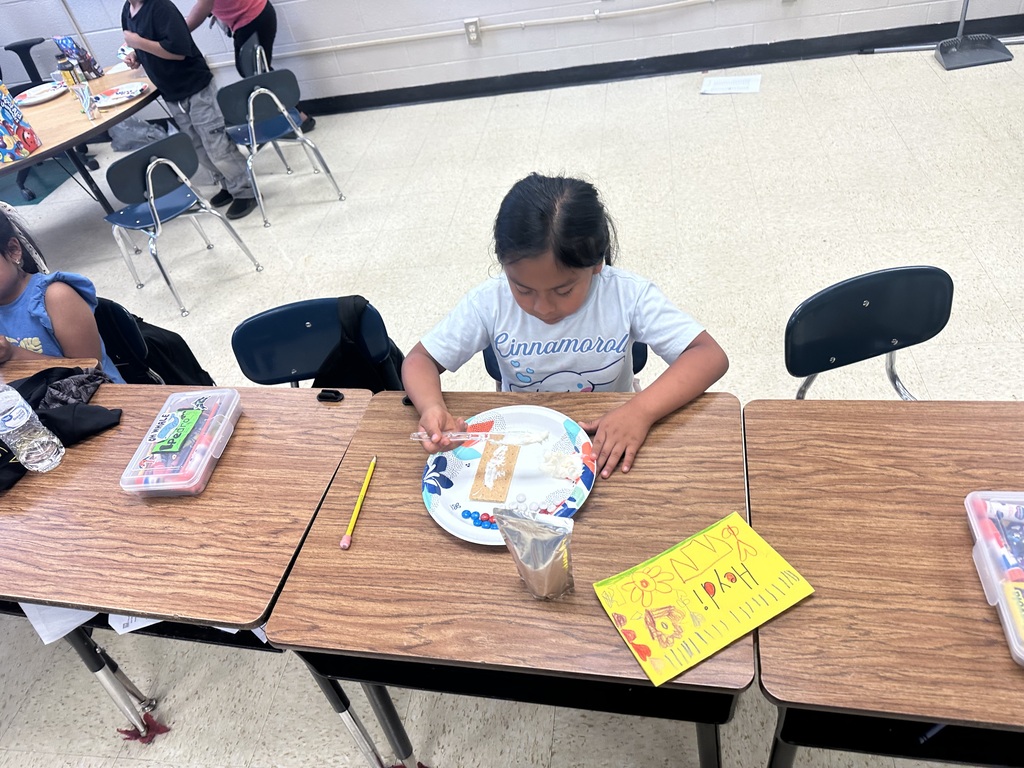 A student is sitting at a desk decorating a graham cracker to look like the American flag.