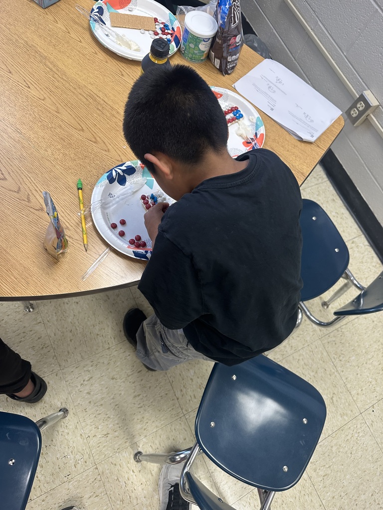 A student is sitting down at a table decorating a graham cracker to look like the American flag.