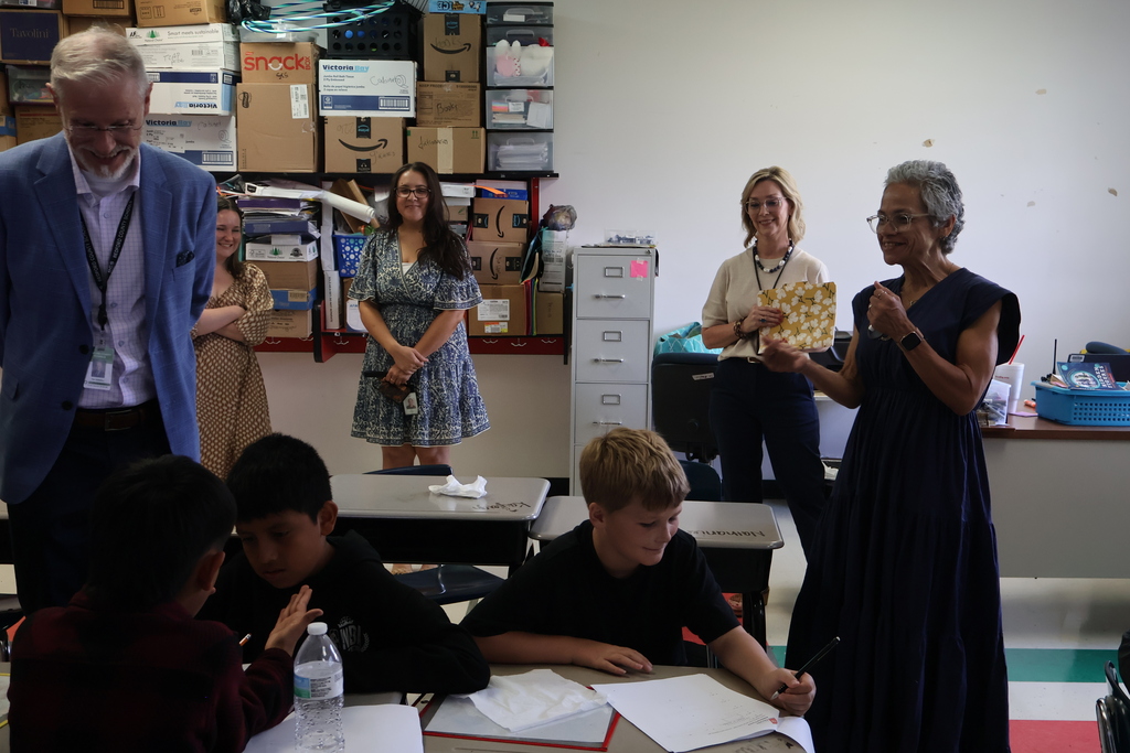 Students are sitting at their desks as the superintendent and commissioner watch them. 