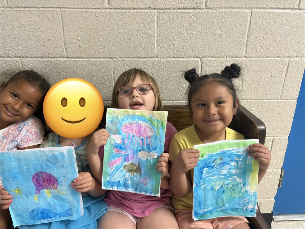 Students are seated on a bench holding up the pictures they created. 