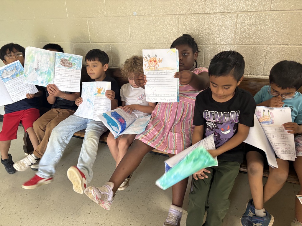 Students are seated on a bench holding up the pictures they created. 