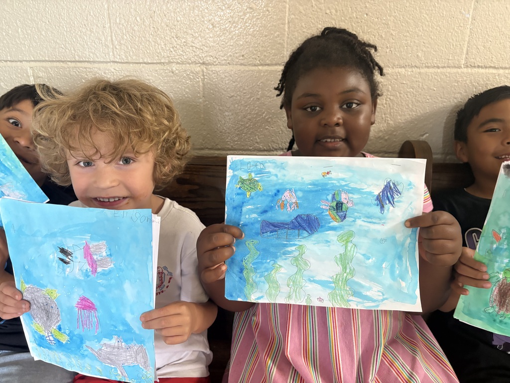 Students are seated on a bench holding up the pictures they created. 