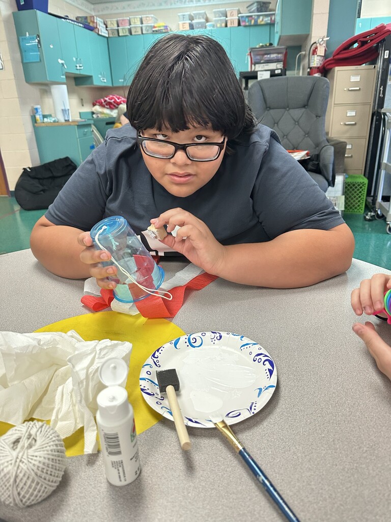 A student is seated at a table working on their flag windsock.