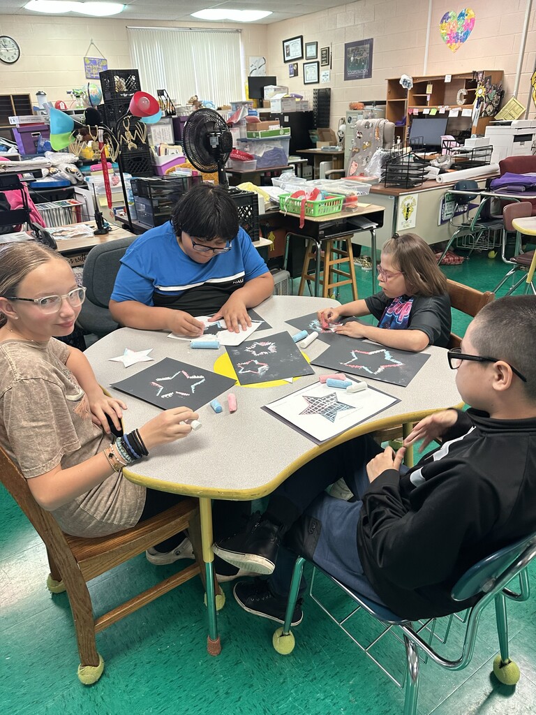 Four students are seated at a table working on artwork that includes a star.