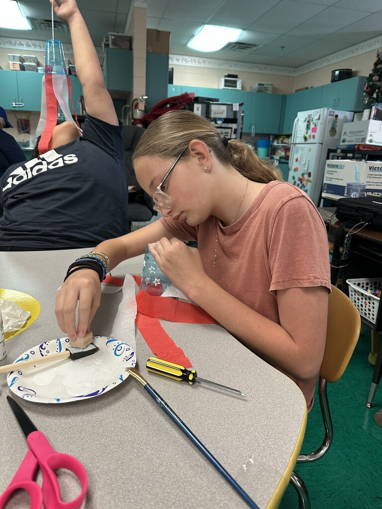 A student is seated at a table working on their flag windsock.