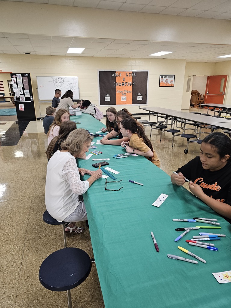 Students are seated at a table with a turquoise tablecloth working on designing their bookmarks.