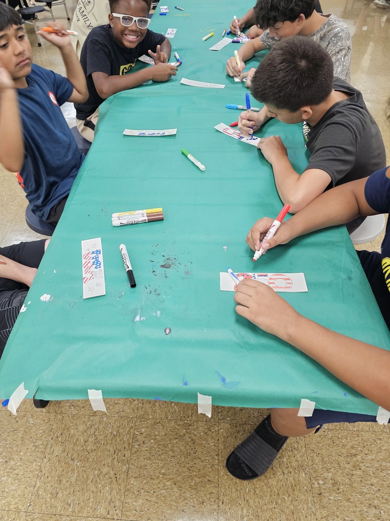 Students are seated at a table with a turquoise tablecloth working on designing their bookmarks.