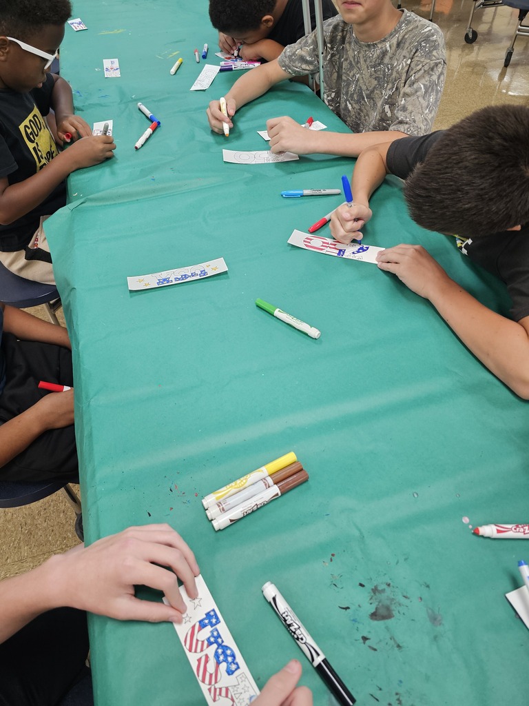 Students are seated at a table with a turquoise tablecloth working on designing their bookmarks.