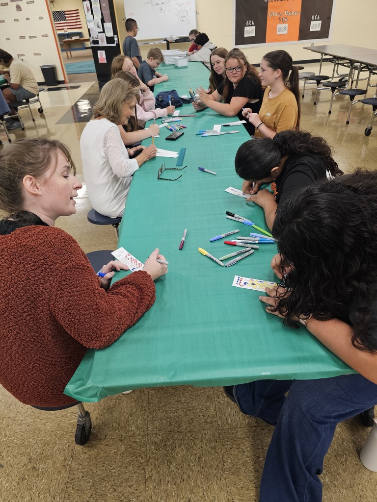 Students are seated at a table with a turquoise tablecloth working on designing their bookmarks.