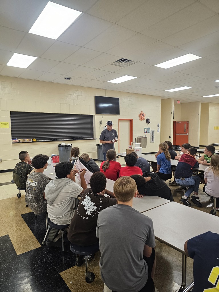 Mr. Shawn Clement from Nash Family Creamery is giving a presentation to students who are seated at cafeteria tables.