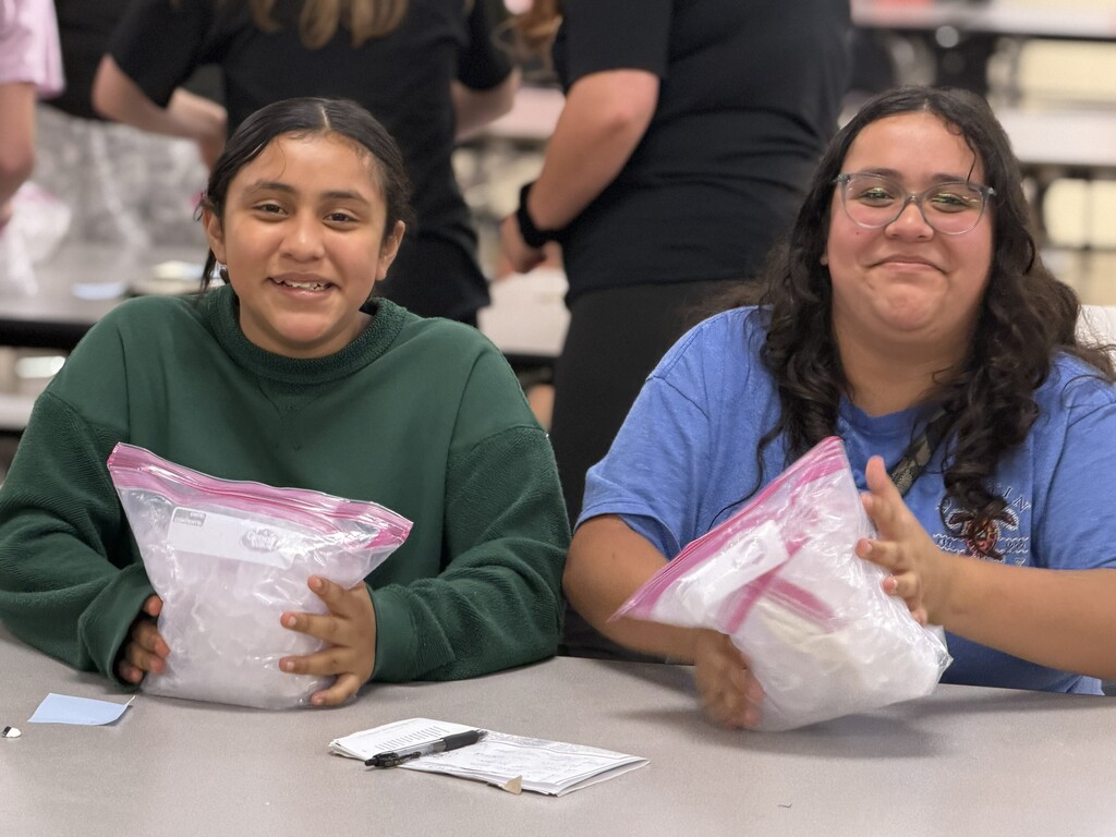 Two students are seated at cafeteria tables as they work on their bags to make ice cream.