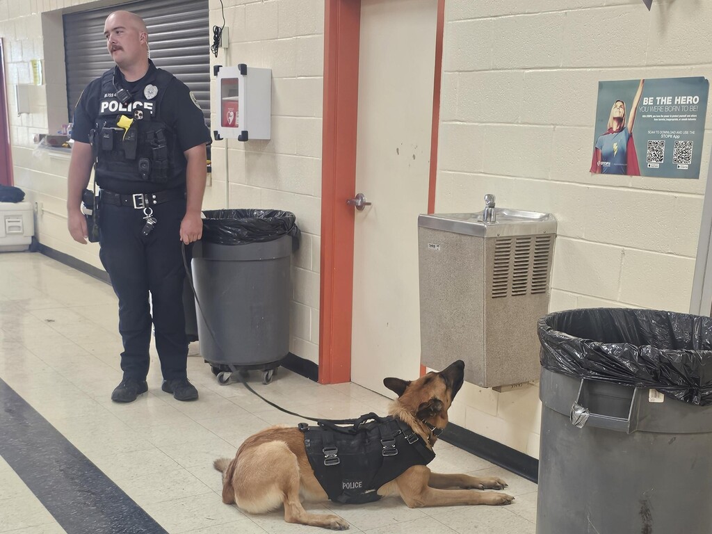 The officer is standing and talking about his K9 to the students.