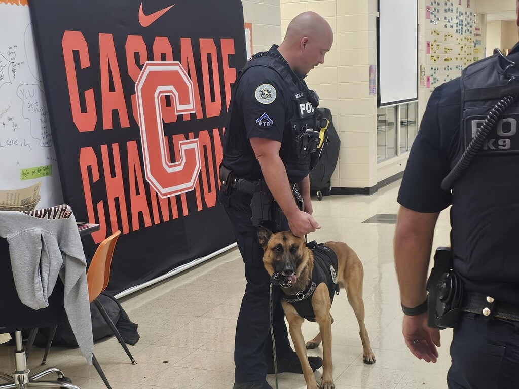 The officer is standing and talking about his K9 to the students.