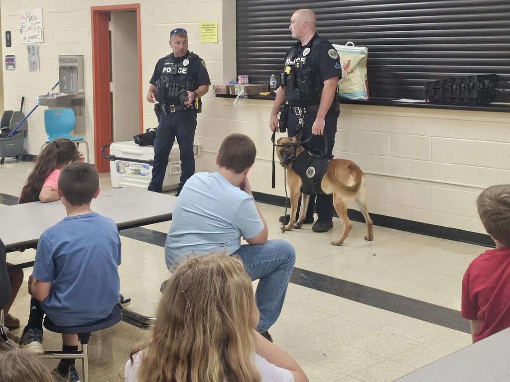 Both of the officers are standing and talking about their K9s to the students.