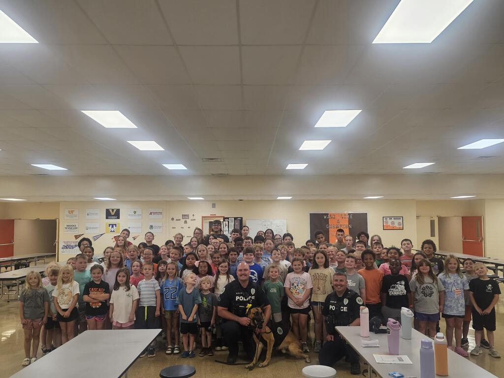 Students are gathered in the cafeteria to take a group picture of the officers and their K9s.