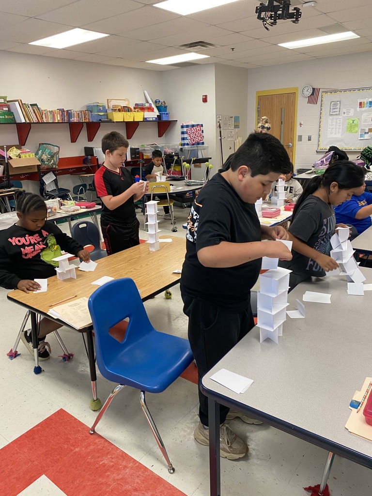 There are several students at their desks building towers out of index cards.