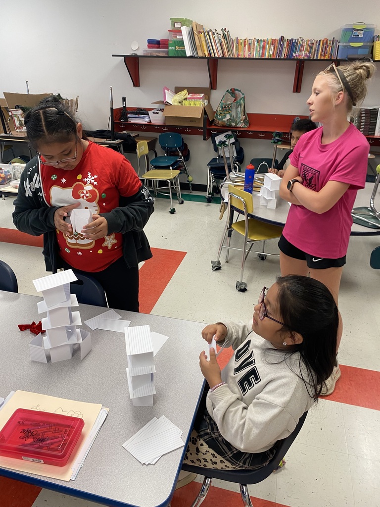 Two students are at their desks building towers out of index cards.