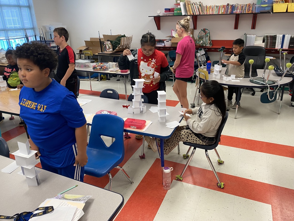 There are several students at their desks building towers out of index cards.