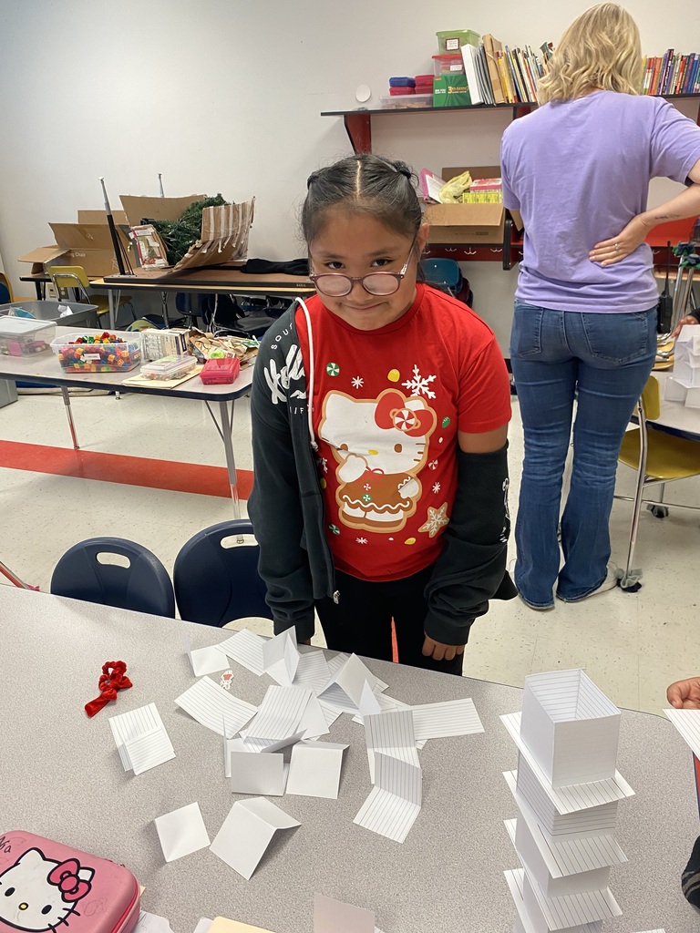 A student is standing at her desk after her tower of index cards fell over.