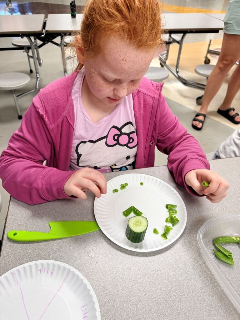 A student is looking down at a plate that has cut up cucumbers on it. 