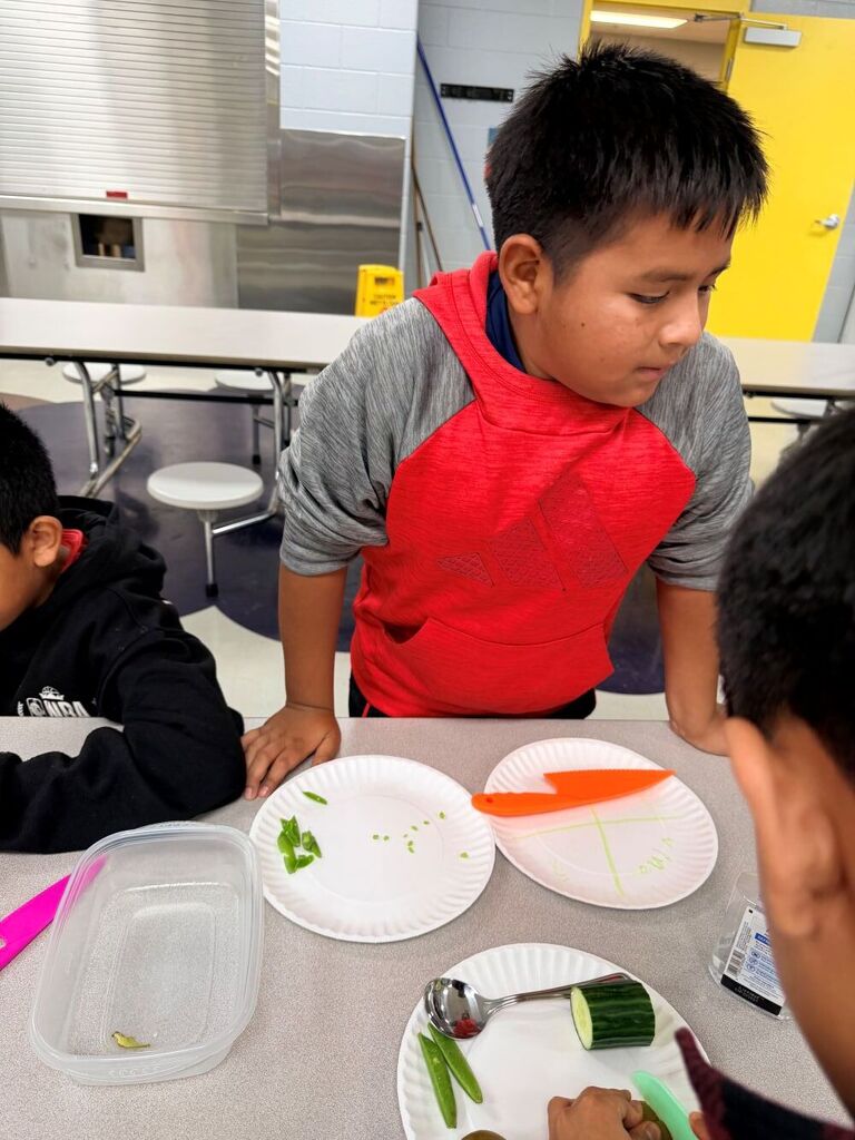 A student is standing at a table helping cut up vegetables.