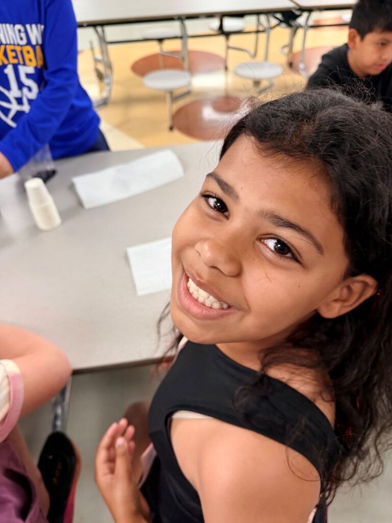 A student is sitting down at a table turned around smiling.