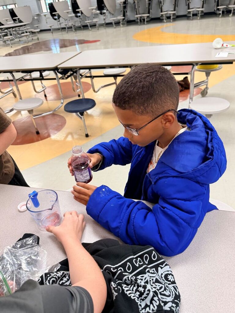 A student is sitting down at a table pouring liquid into a cup.