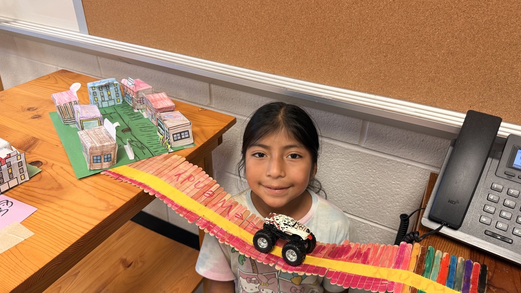 A student is standing beside the table testing out her bridge with a toy car.