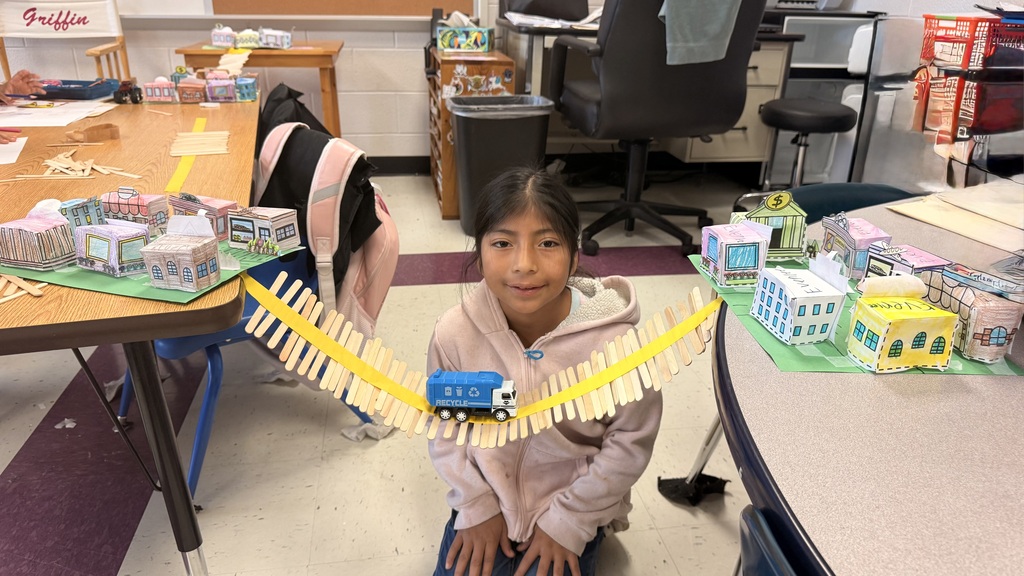 A student is standing beside the table testing out her bridge with a toy car.