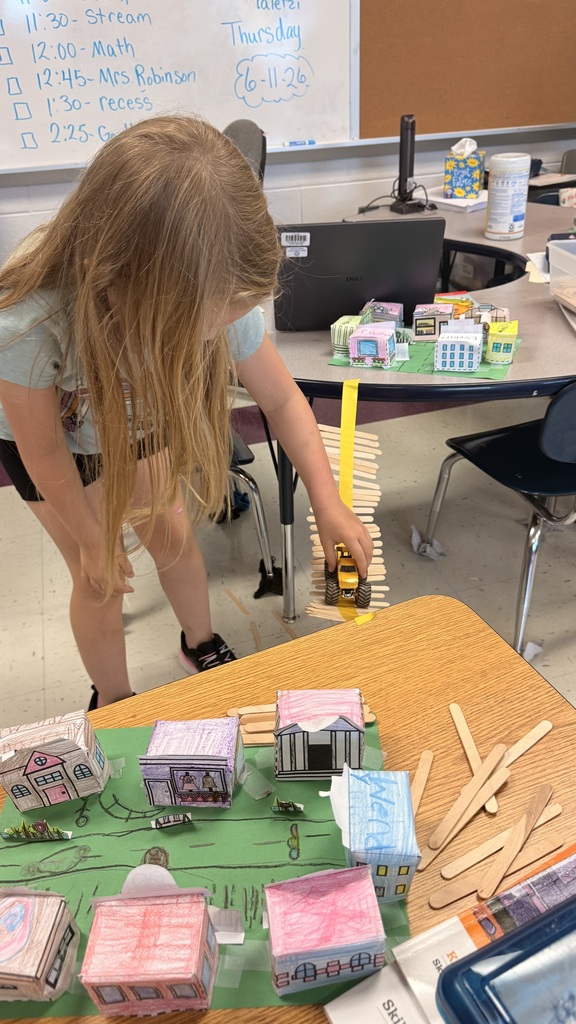 A student is standing beside the table testing out her bridge with a toy car.