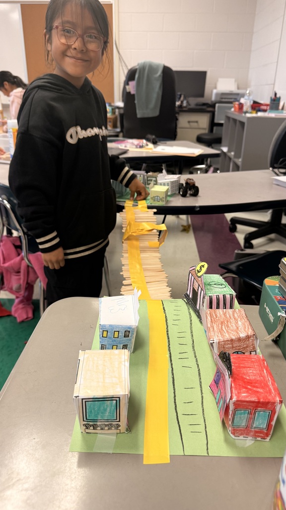 A student is standing beside the table testing out her bridge with a toy car.