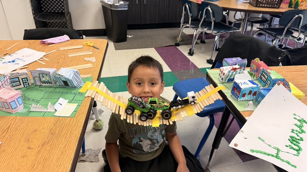 A student is standing beside the table testing out his bridge with a toy car.